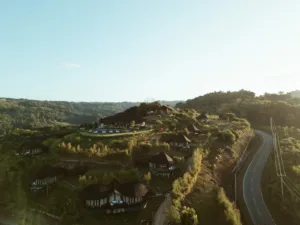 Aerial view of bamboo-roofed villas beside a curving road in the hills of West Sumba.