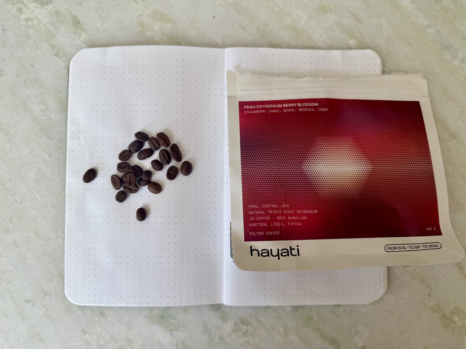 Hyalti dried cherry blossom tea in a red and white packet with coffee beans on a white dotted notebook.