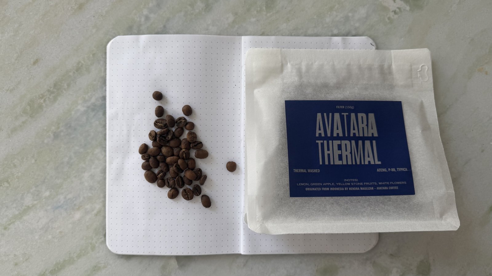 Close-up of Avatar Thermal coffee packets and coffee beans on a white surface, showcasing the product and ingredients.